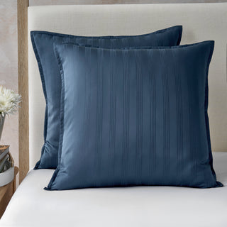 Two blue pillows on a bed with a neutral headboard.
