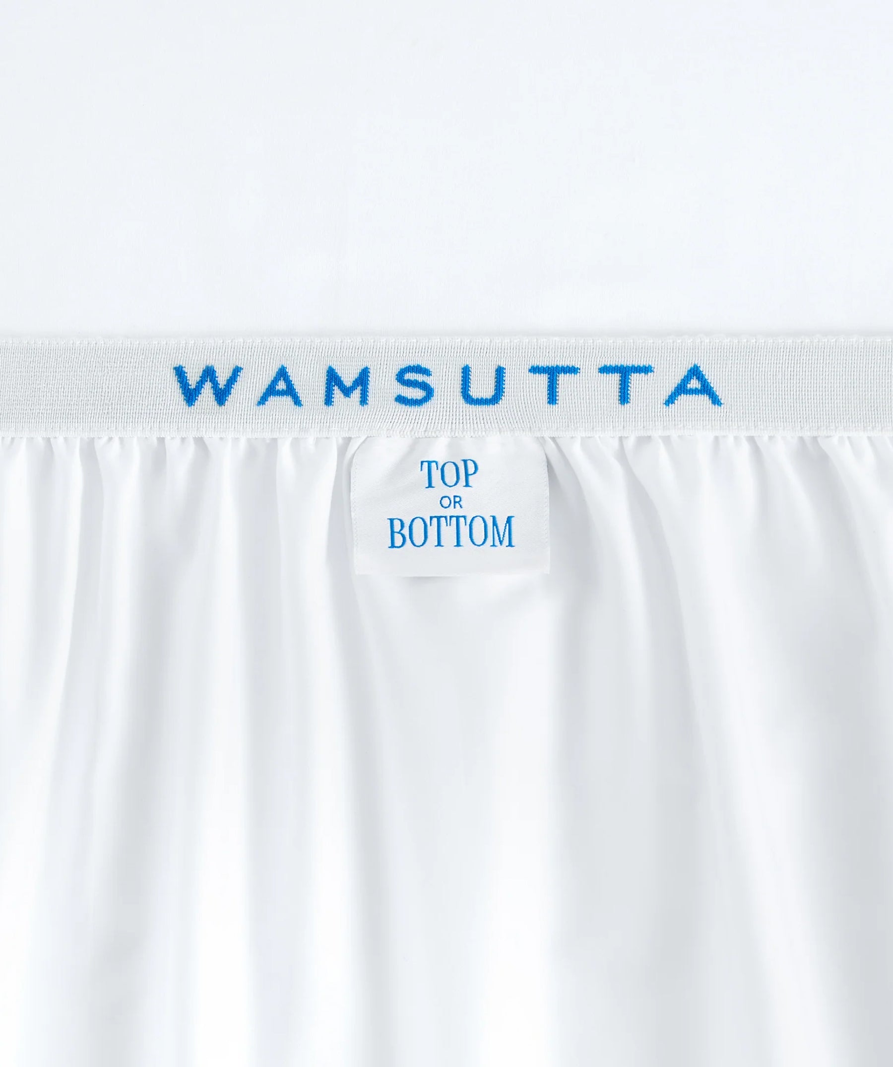 Close-up of white fitted sheet with Wamsutta branding and top-or-bottom label.