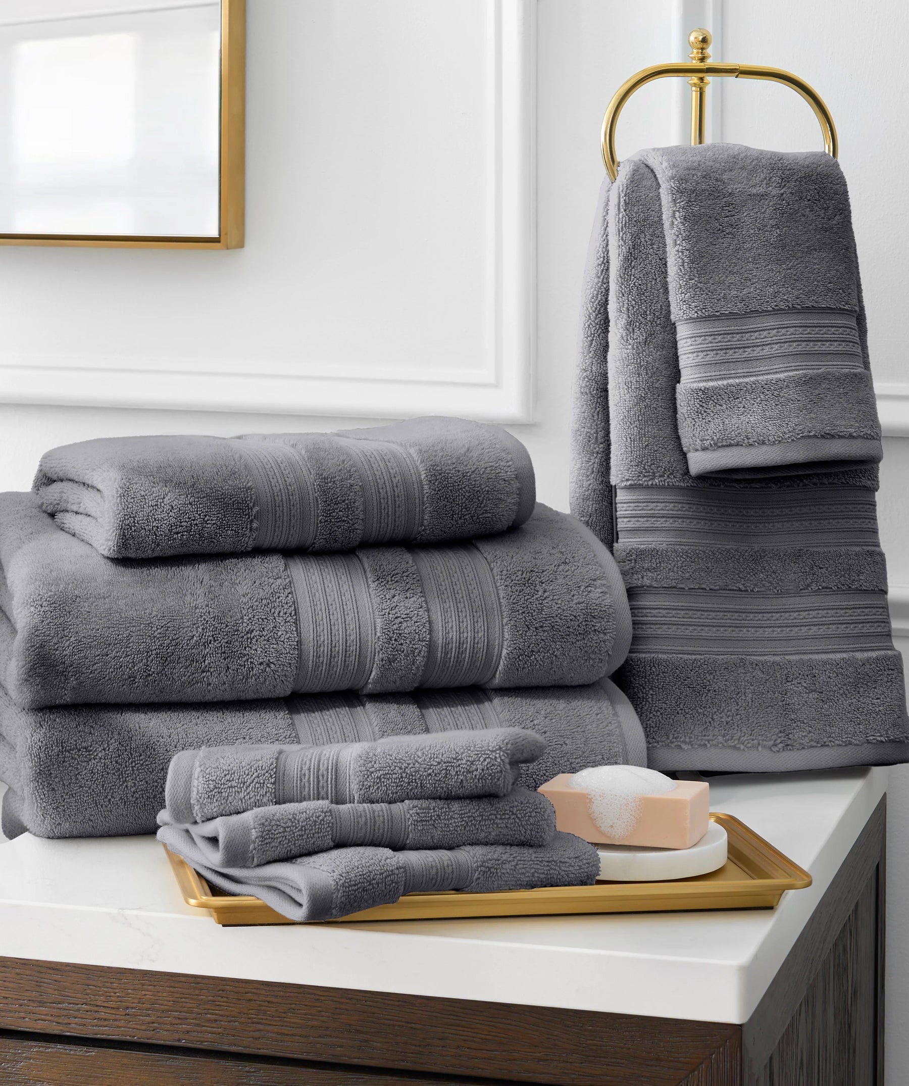 Gray bath towel collection displayed on a bathroom vanity with folded towels and a towel stand.