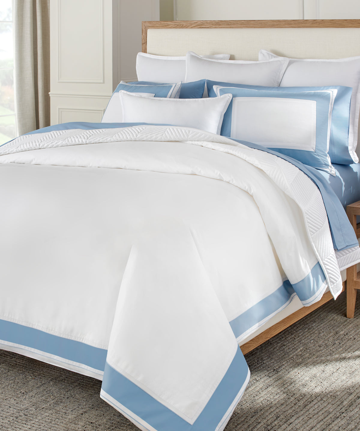 White and blue bedding set on a bed with a wooden headboard.
