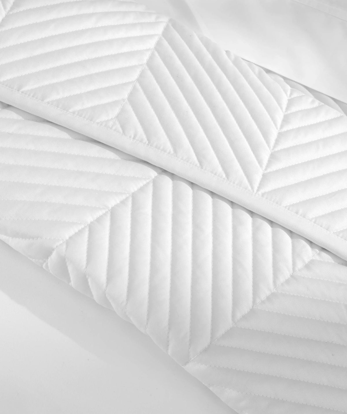 Close-up of herringbone stitch quilting on a white coverlet.