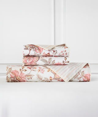 Three folded sheets with a floral and botanical print in pink, beige, and brown, stacked on a white surface against a white paneled wall.