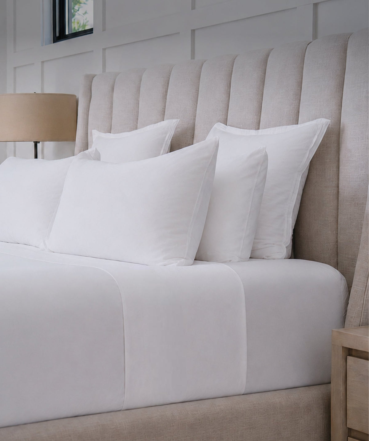 White cotton fitted sheet styled on a bed with white pillows.