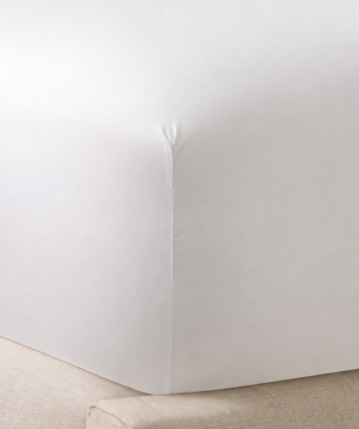 Close-up of a white fitted sheet secured around a mattress corner.