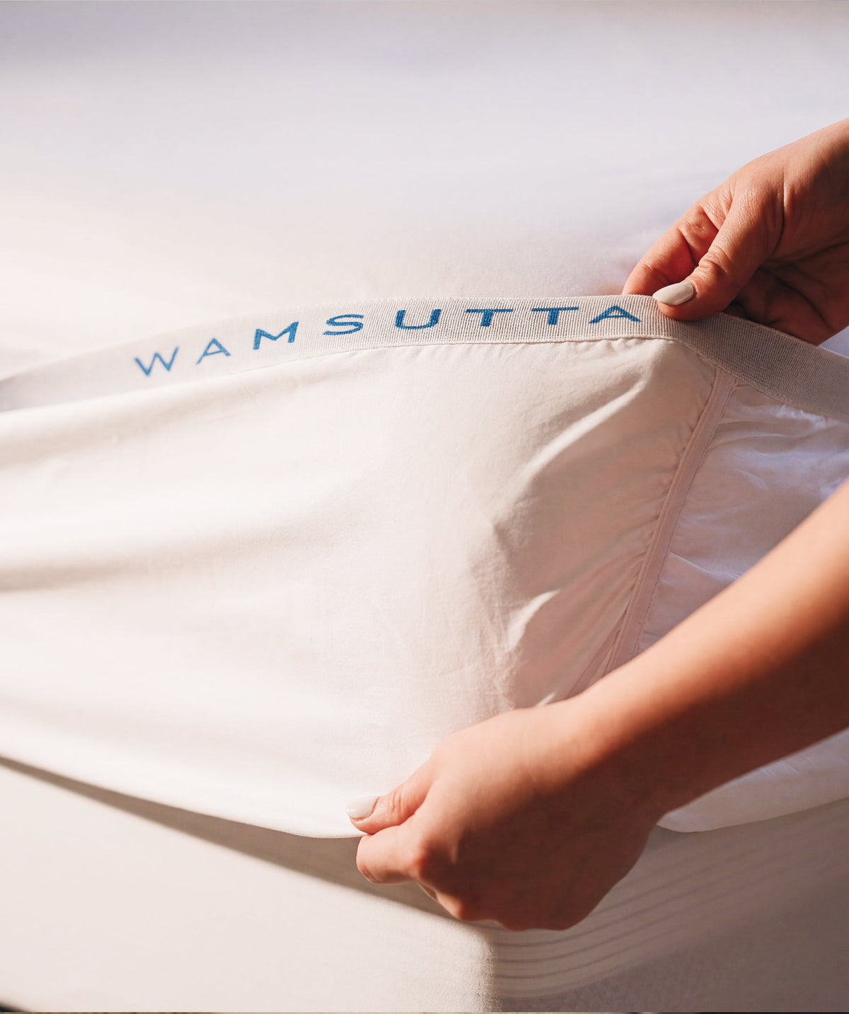 Person fitting a white cotton fitted sheet over a mattress.