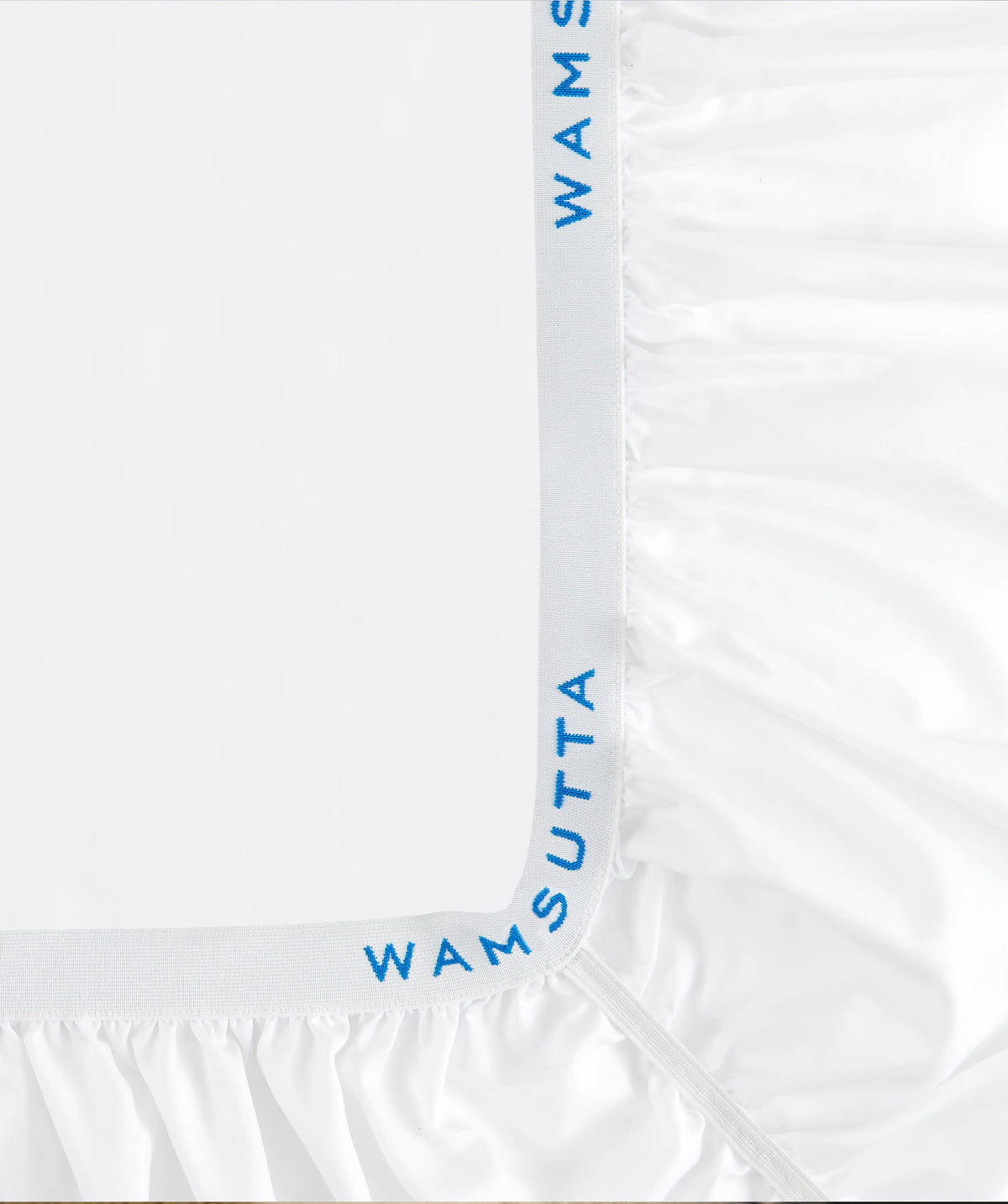 Close-up of the elastic edge and Wamsutta logo on a white fitted sheet.