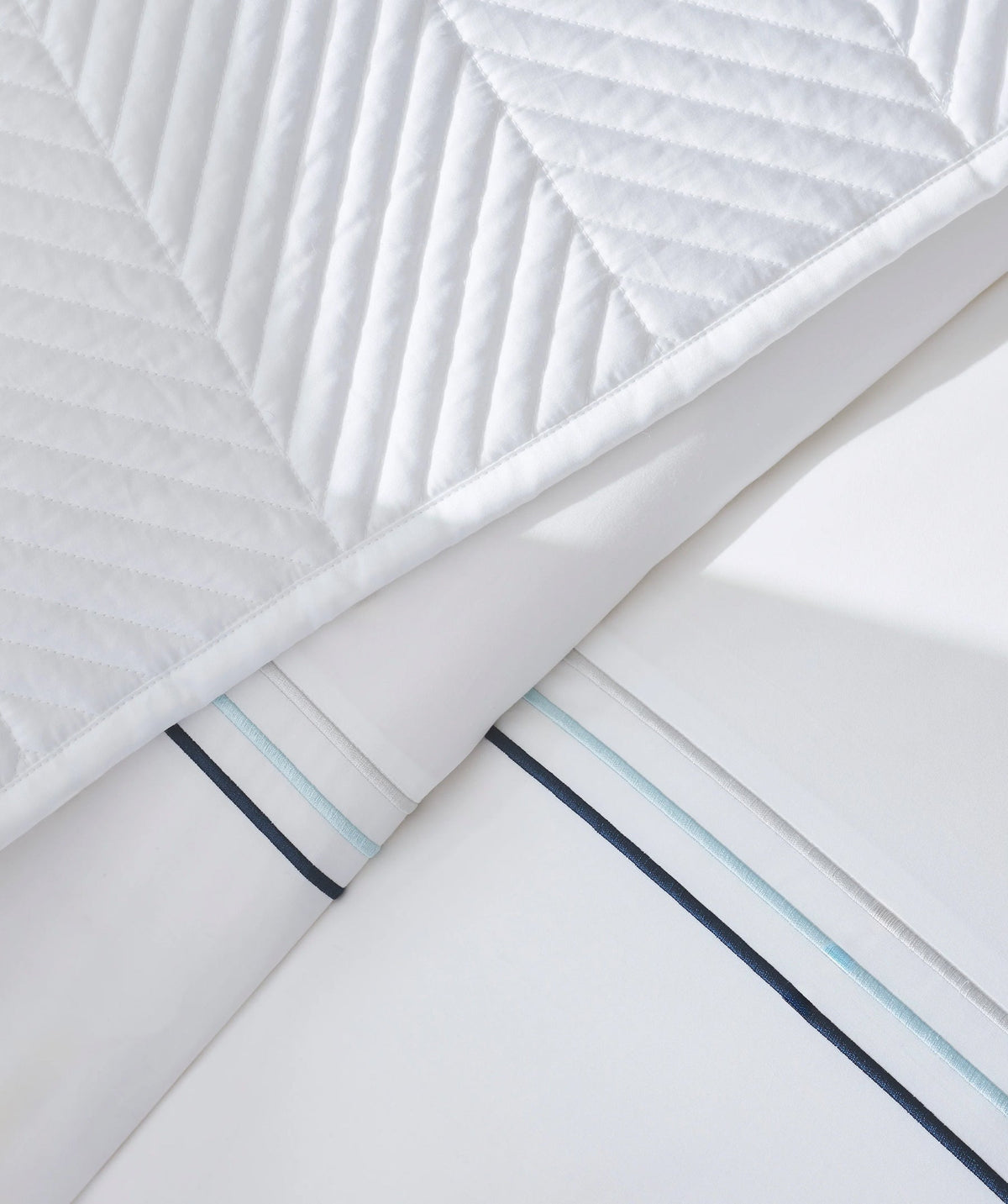 Close-up of white embroidered border bedding with a quilted coverlet.