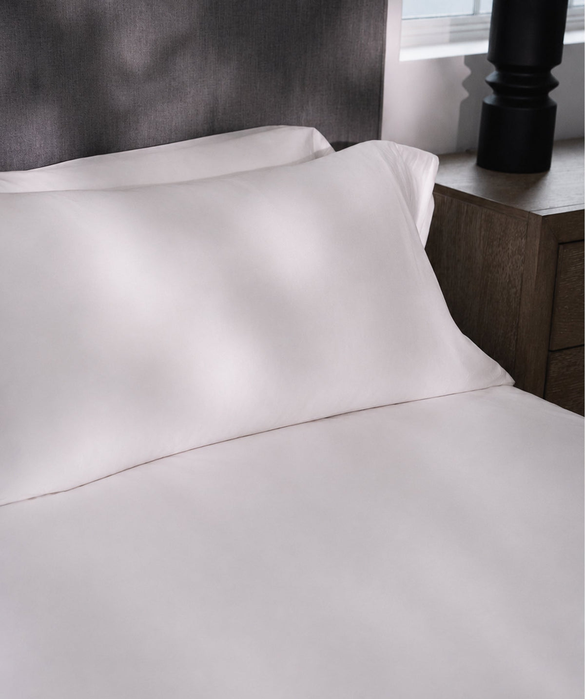 White pillowcase styled on a bed beside a dark wood nightstand.