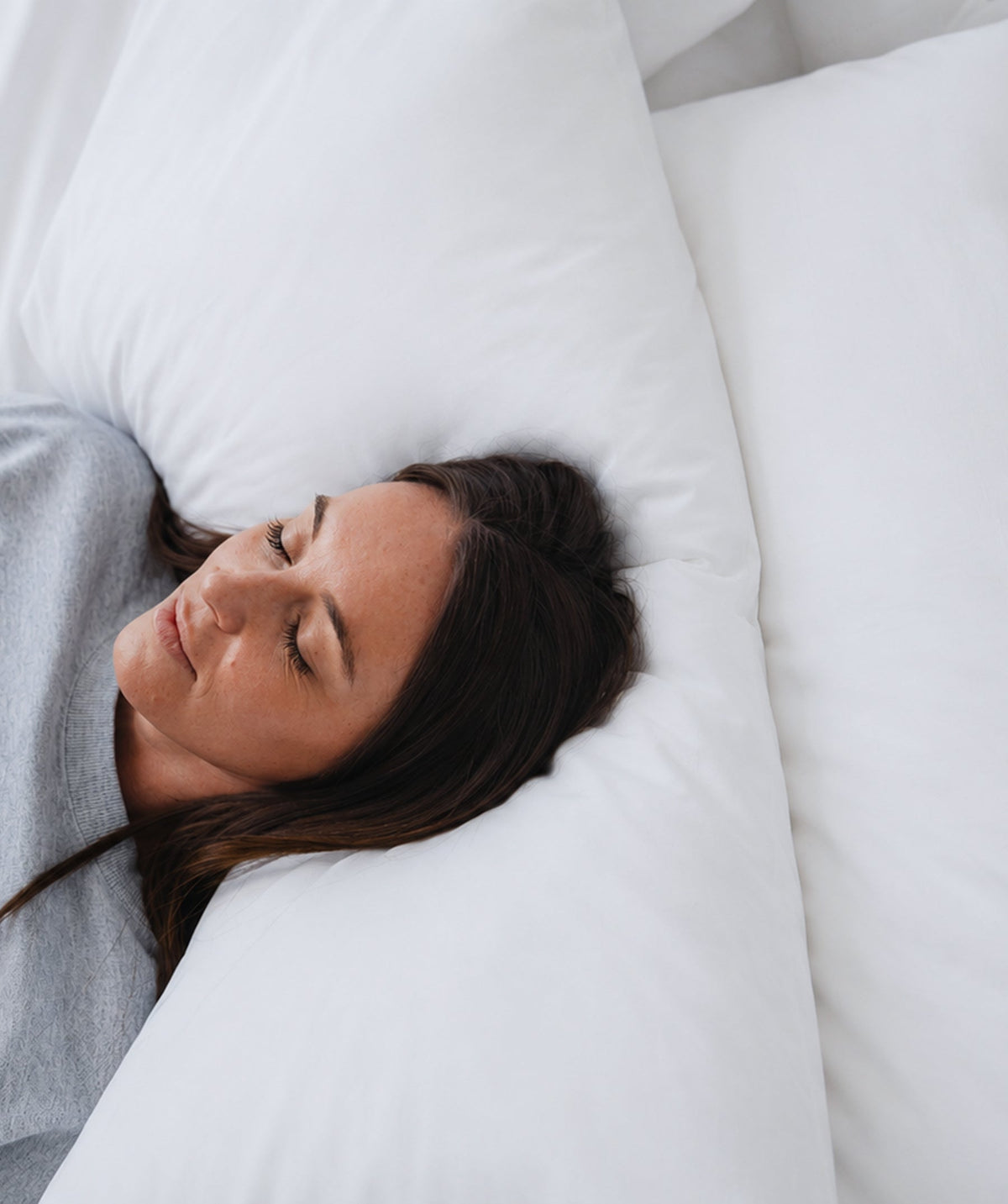 Woman resting with her head on a soft white pillowcase.