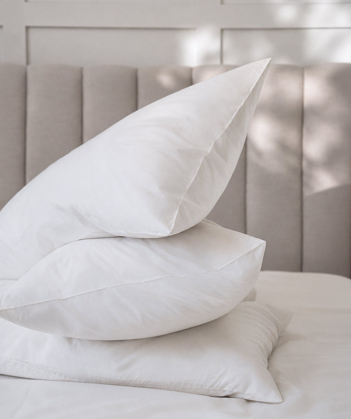 Stack of crisp white pillows styled on a neatly made bed.