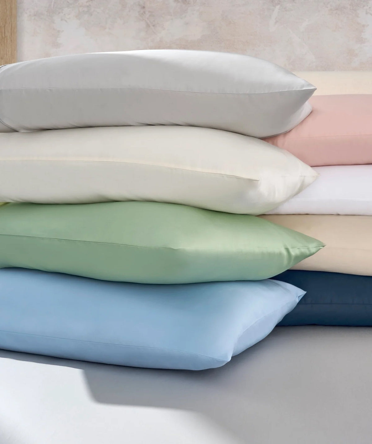 Stacked pillowcases in an assortment of soft neutral, blue, green, and pink colors.