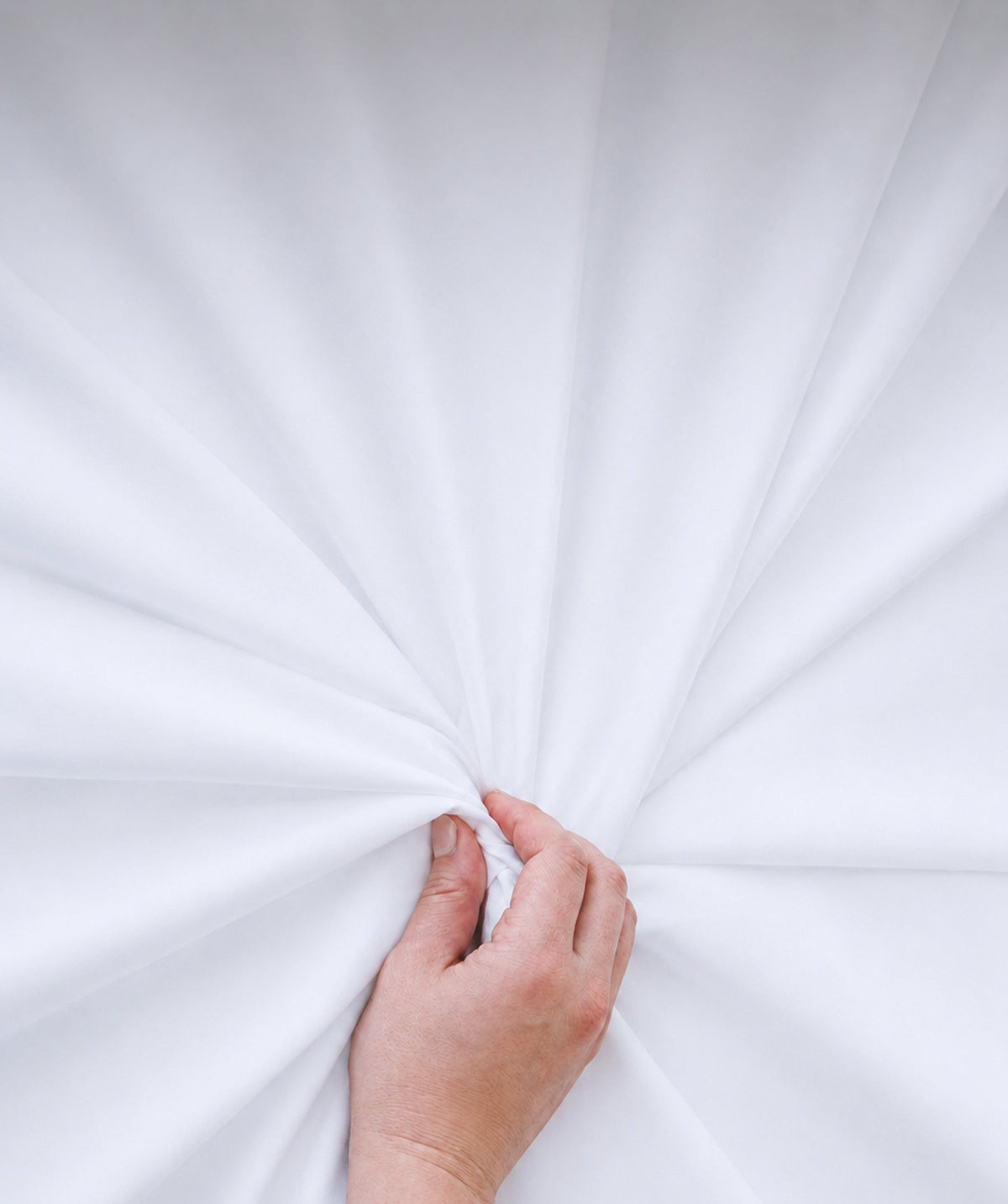 Hand gathering soft white sheet fabric to highlight its smooth texture and drape.