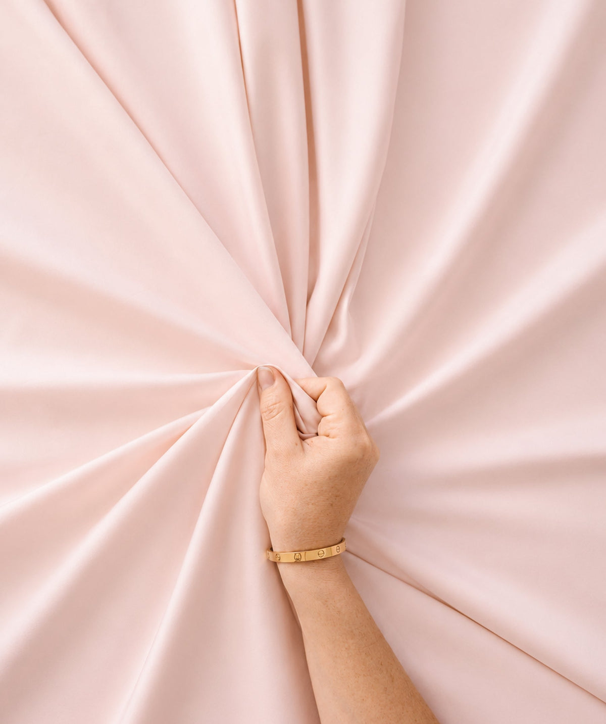 Hand gathering soft pink sheet fabric to highlight its smooth texture and drape.