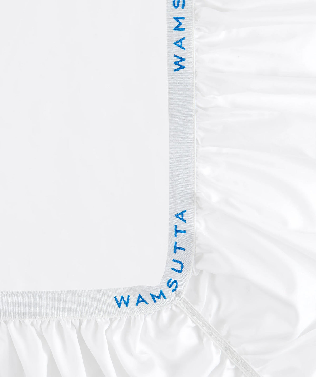 Close-up of a white fitted sheet corner with branded elastic and gathered fabric.