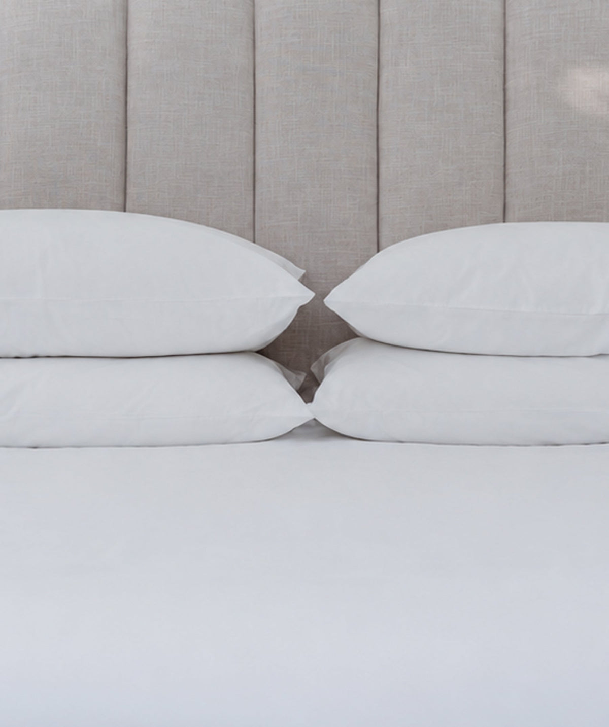 Four white pillows neatly arranged against a neutral upholstered headboard.