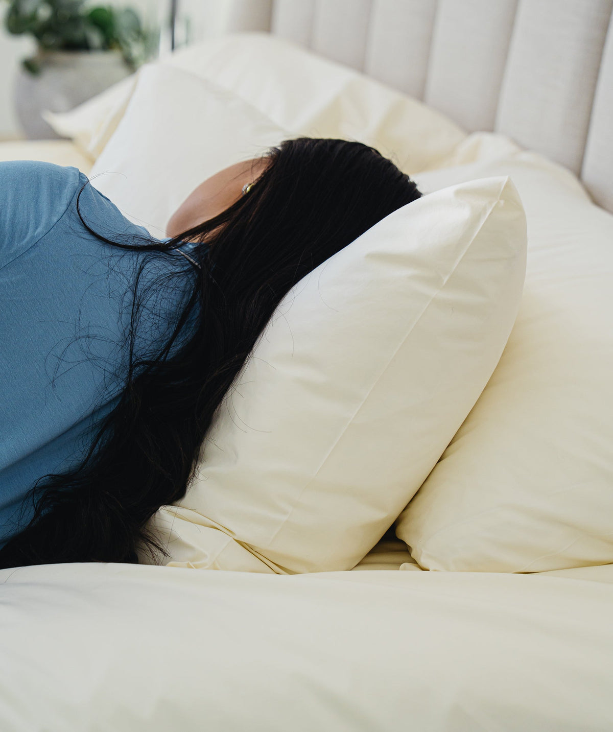 Person resting on soft ivory pillowcases in a bright bedroom.