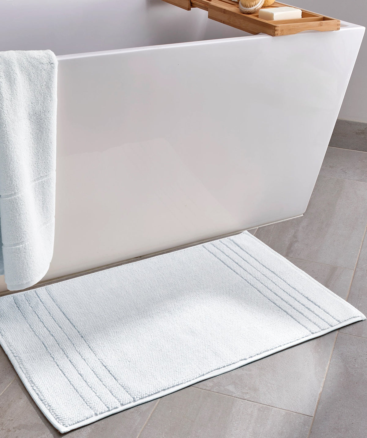 White bath mat placed beside a freestanding bathtub.