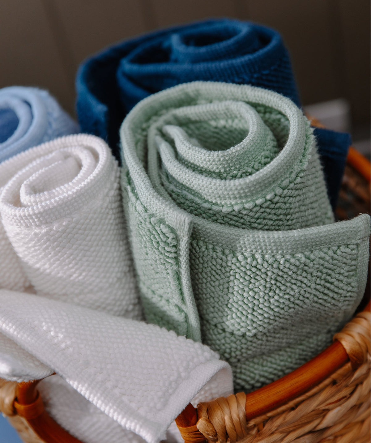 Rolled bath mats in assorted colors in a woven basket.
