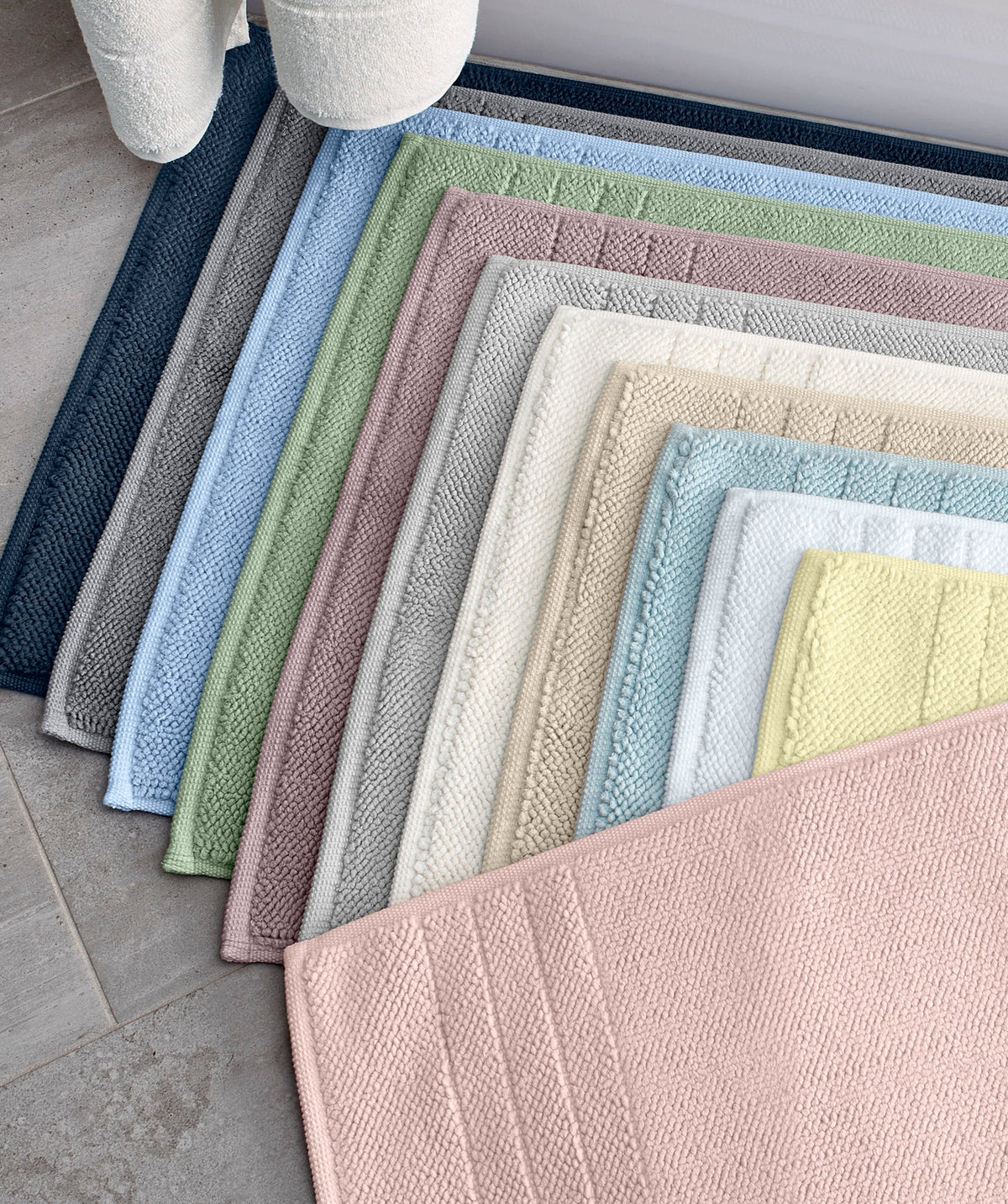 Bath mats in assorted colors displayed beside a bathtub.