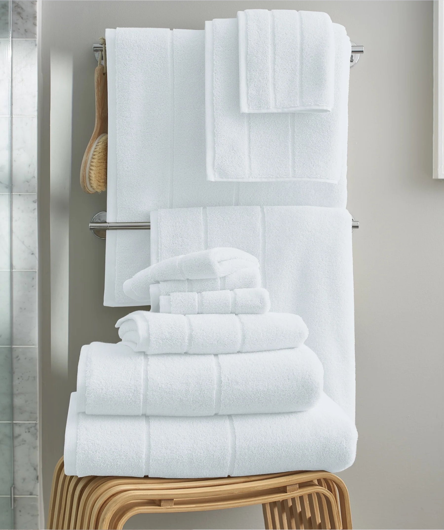 White bath sheet collection displayed on a towel rack with folded towels and a bath brush.