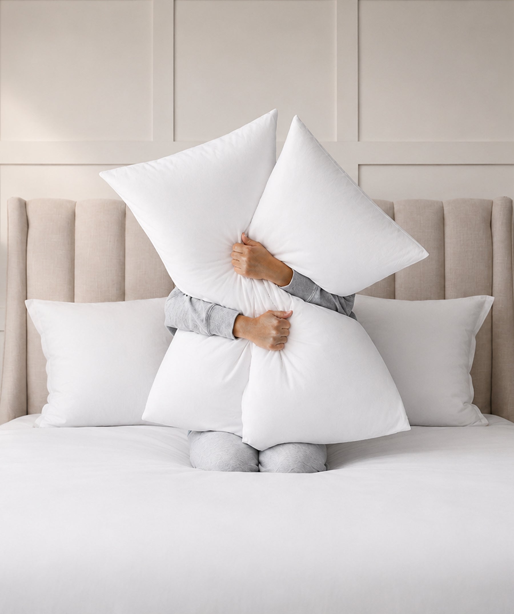 Person hugging two white bed pillows while sitting on a bed.