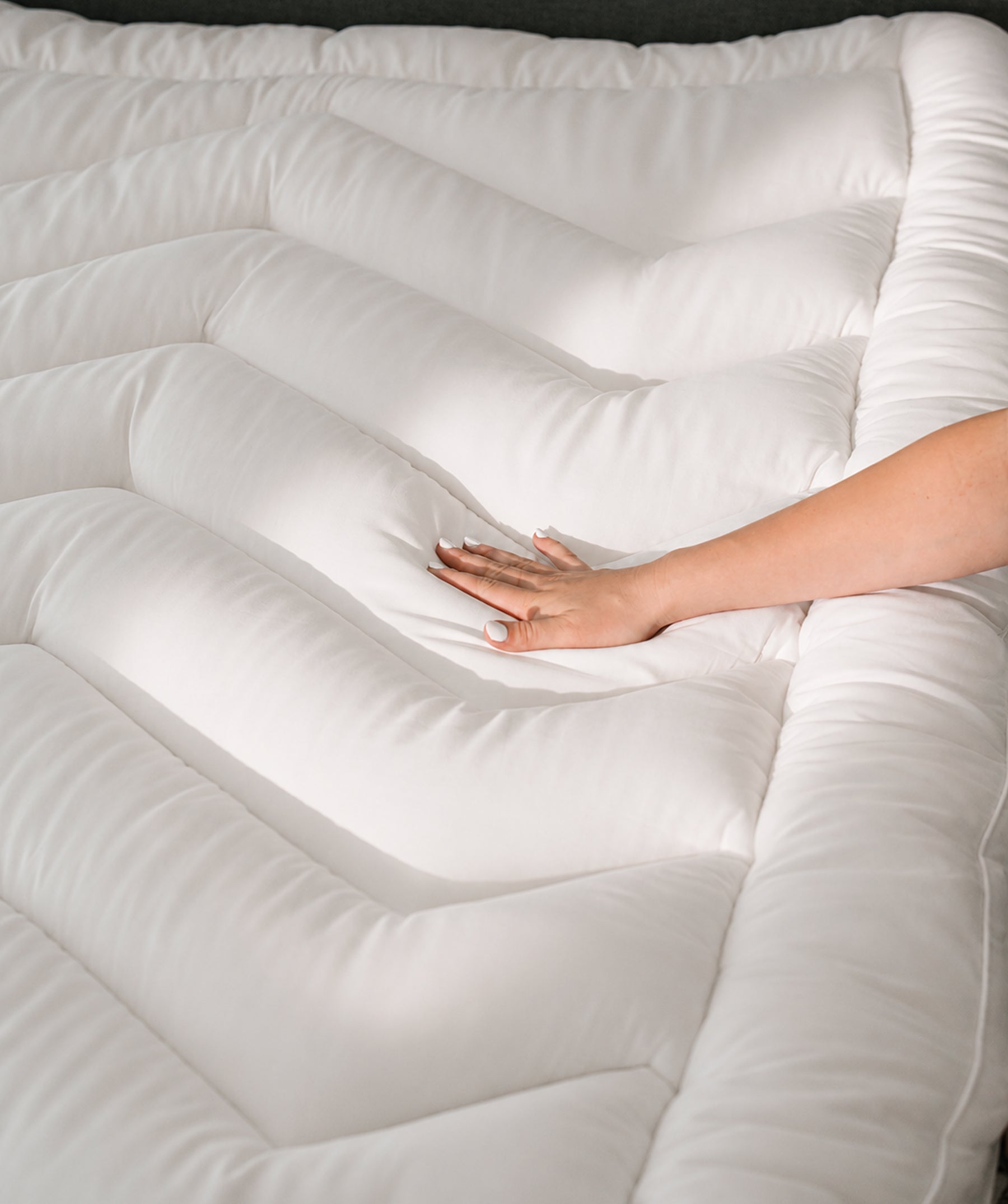 Hand pressing into a white pillow top mattress topper.