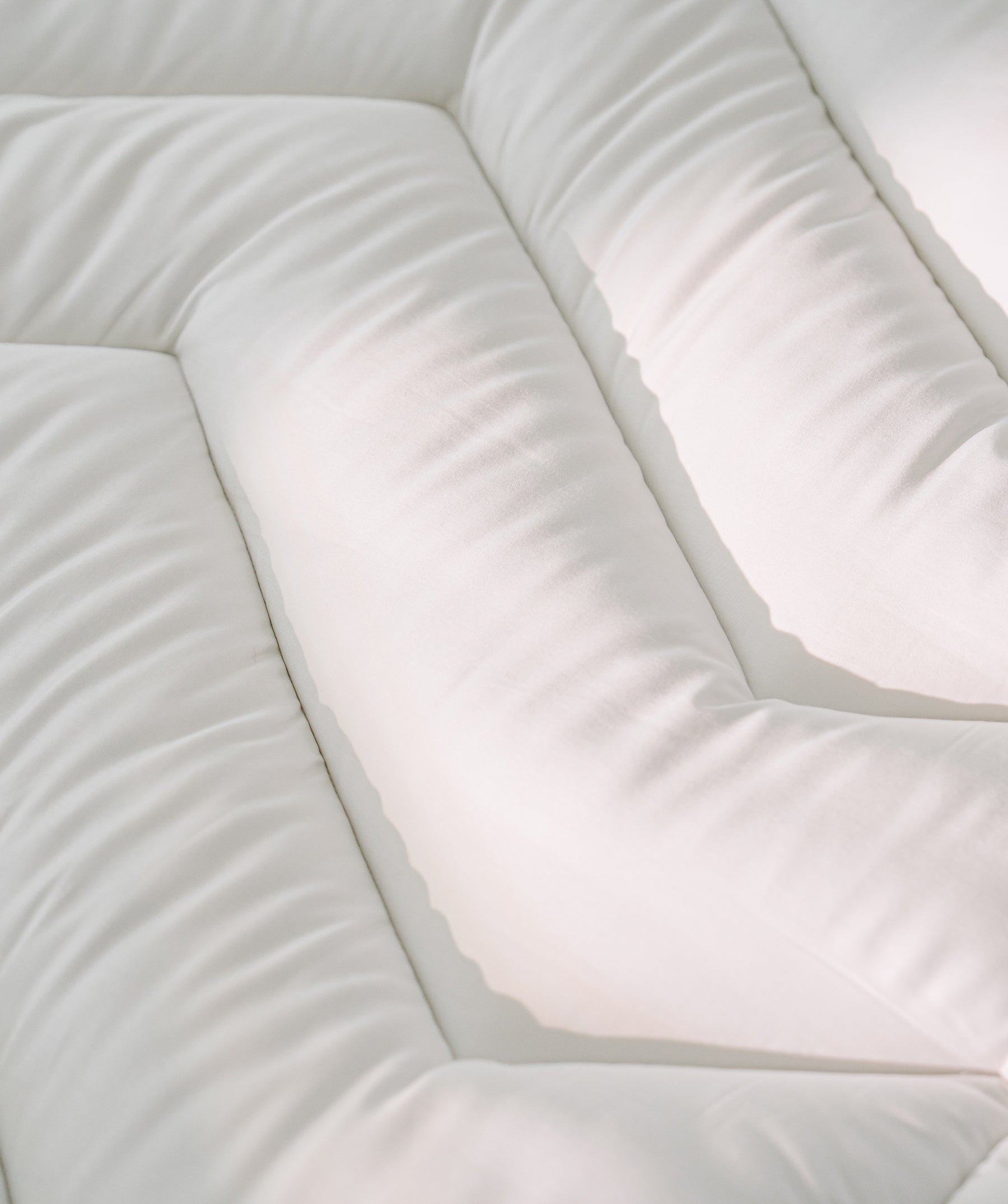Close-up of quilted channels on a white pillow top mattress topper.