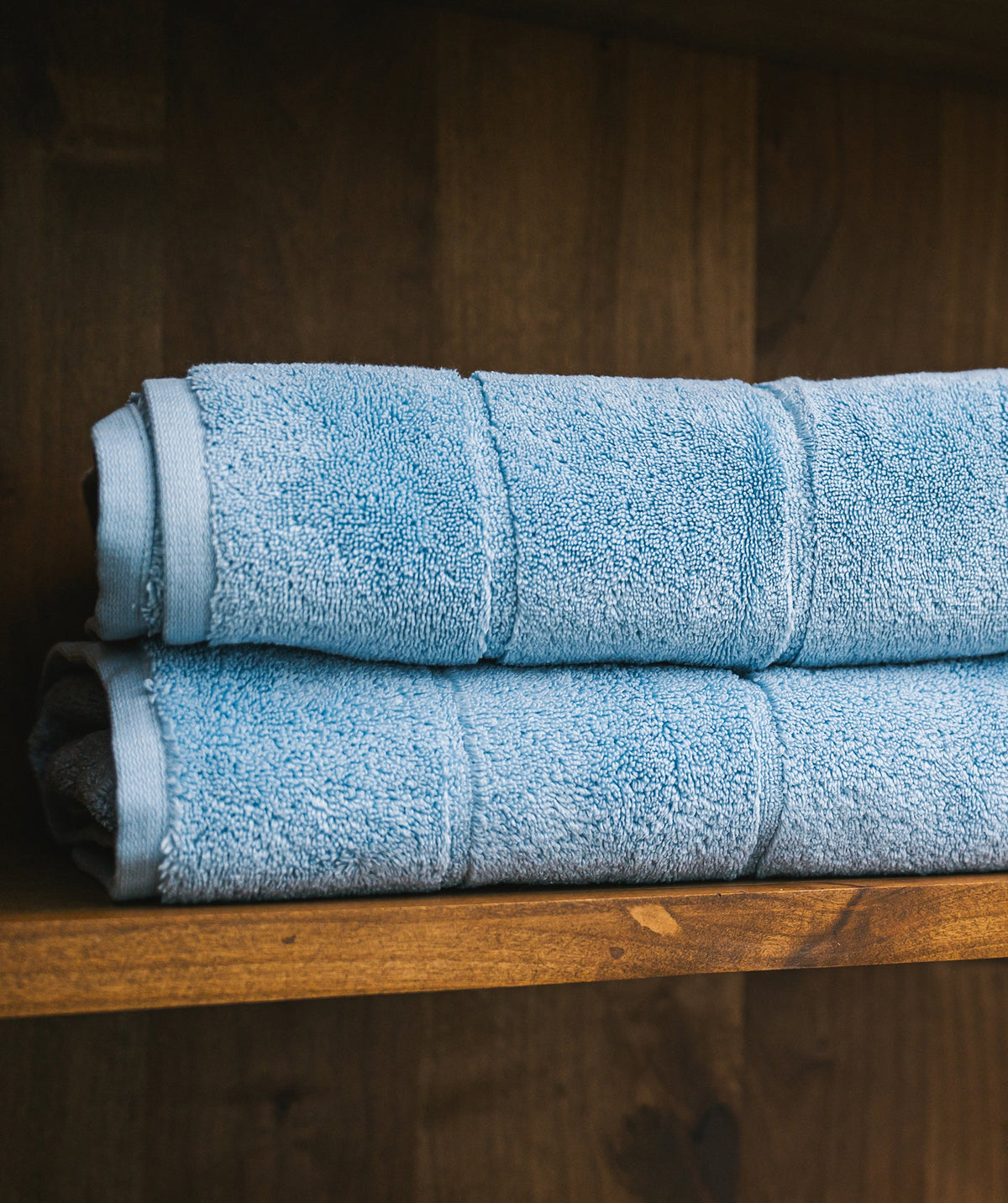 Two blue Egyptian cotton bath towels folded on a wooden bathroom shelf.