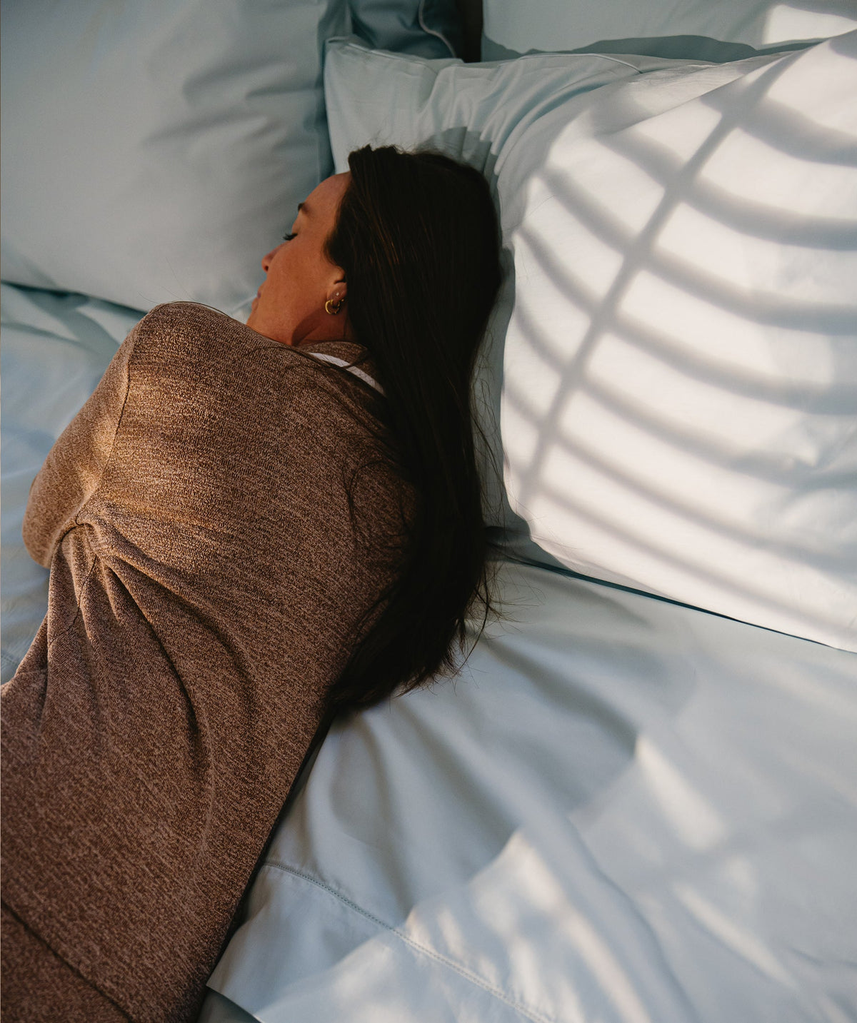 Person resting on white pillows and bedding in warm natural light.