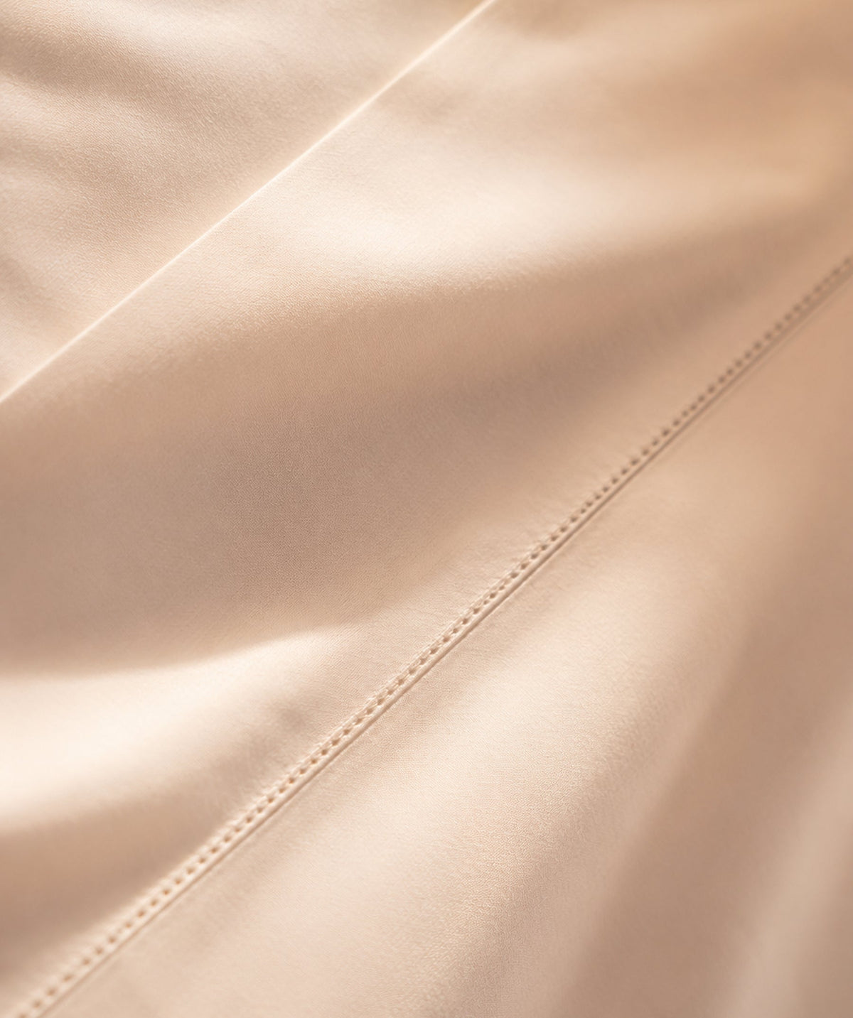 Close-up of smooth beige sheet fabric with decorative stitching.