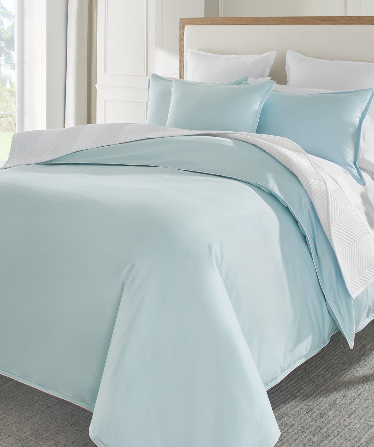 Light blue sateen comforter set on a bed with pillows in a bright room.