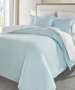 Light blue sateen comforter set on a bed with pillows in a bright room.