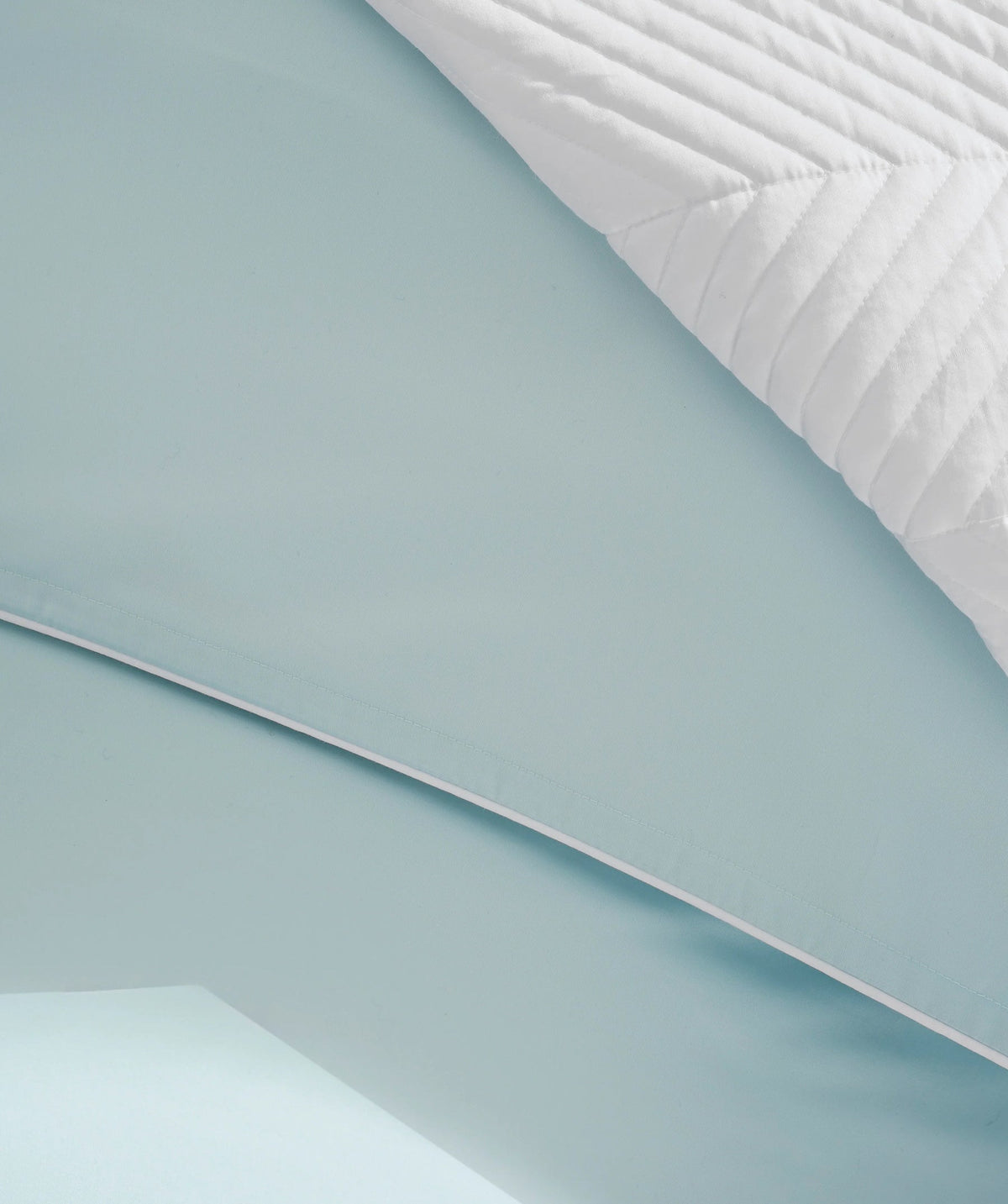 Close-up of a pastel blue solid duvet cover with white piping.