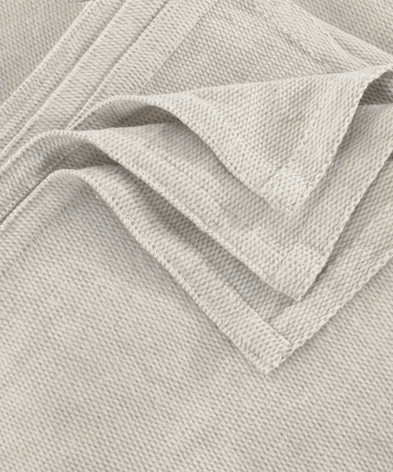 A close-up of a light beige woven fabric with a textured basketweave pattern, folded to show the material's texture and color.