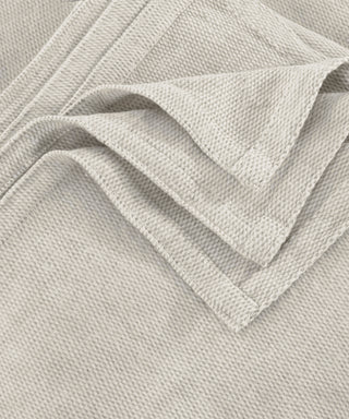 A close-up of a light beige woven fabric with a textured basketweave pattern, folded to show the material's texture and color.