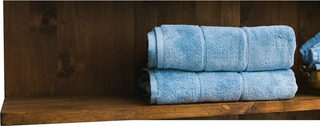 Folded blue Wamsutta towels on a wooden shelf